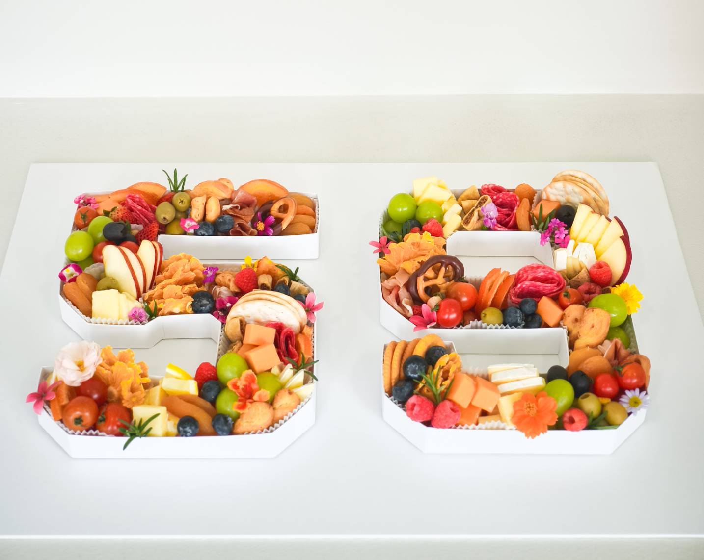 Custom letter S snack box with cheese, fruits, cold cuts, nuts, and decorated with edible flowers