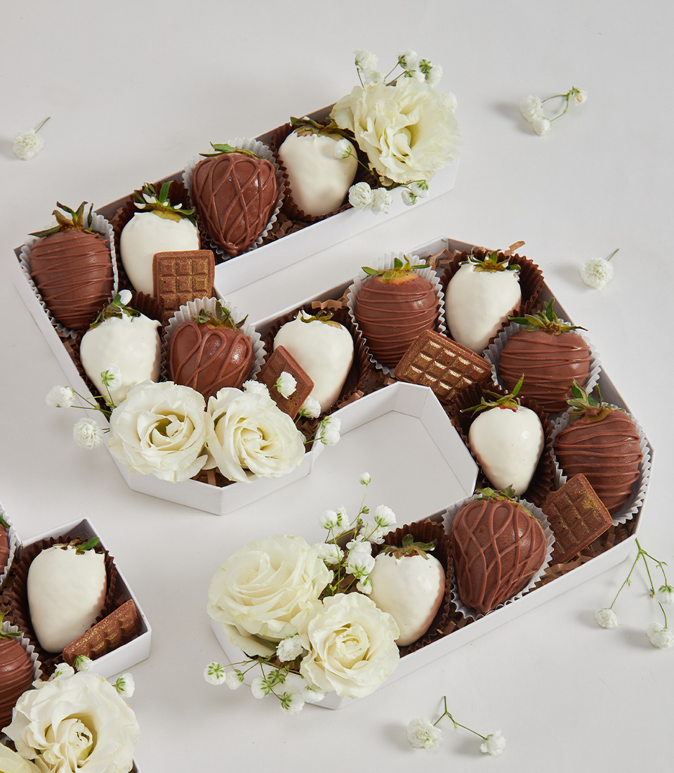 Close-up of number 5 box with white and chocolate-covered strawberries, golden chocolate wafers, and white roses on a clean background
