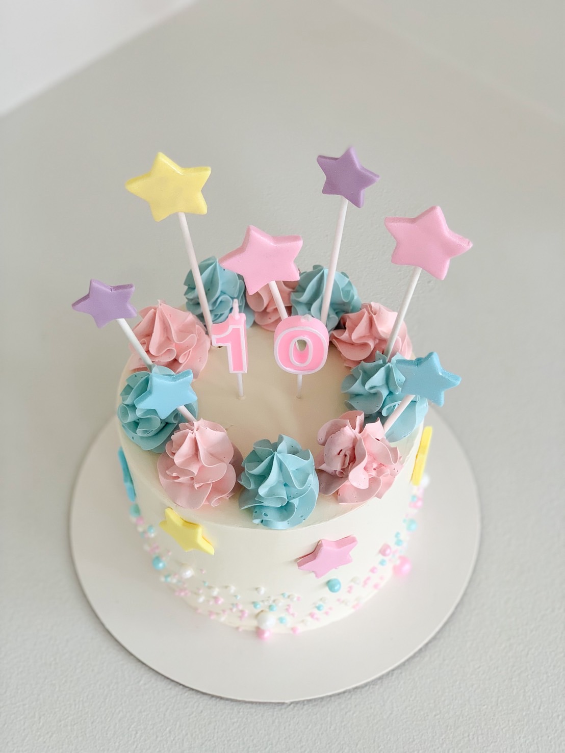 Top view of pastel star birthday cake with pink number 10 topper, colourful fondant stars, and pastel buttercream swirls for kids.