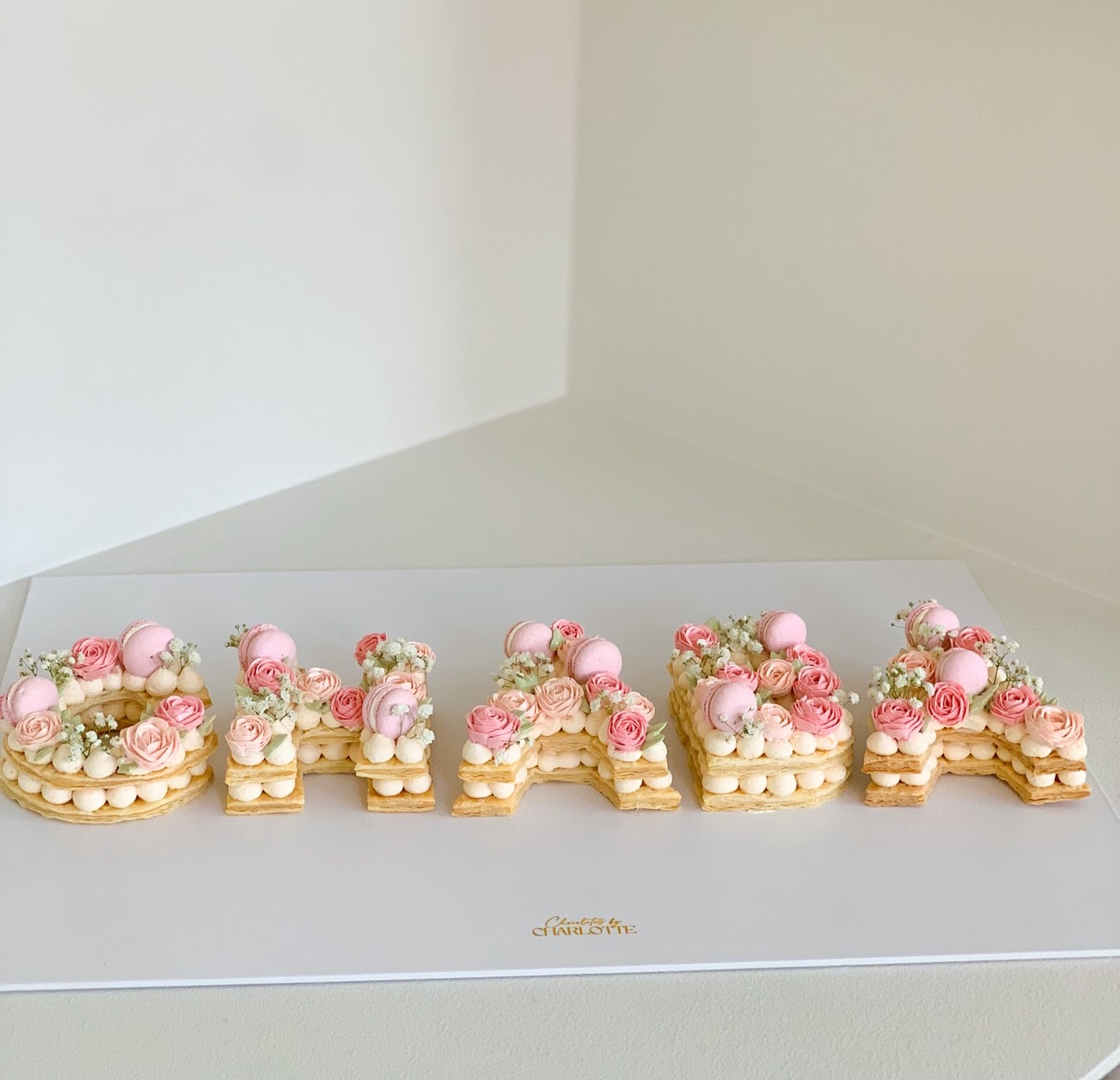 Custom letter and number cream tart cake decorated with pink roses and macarons.