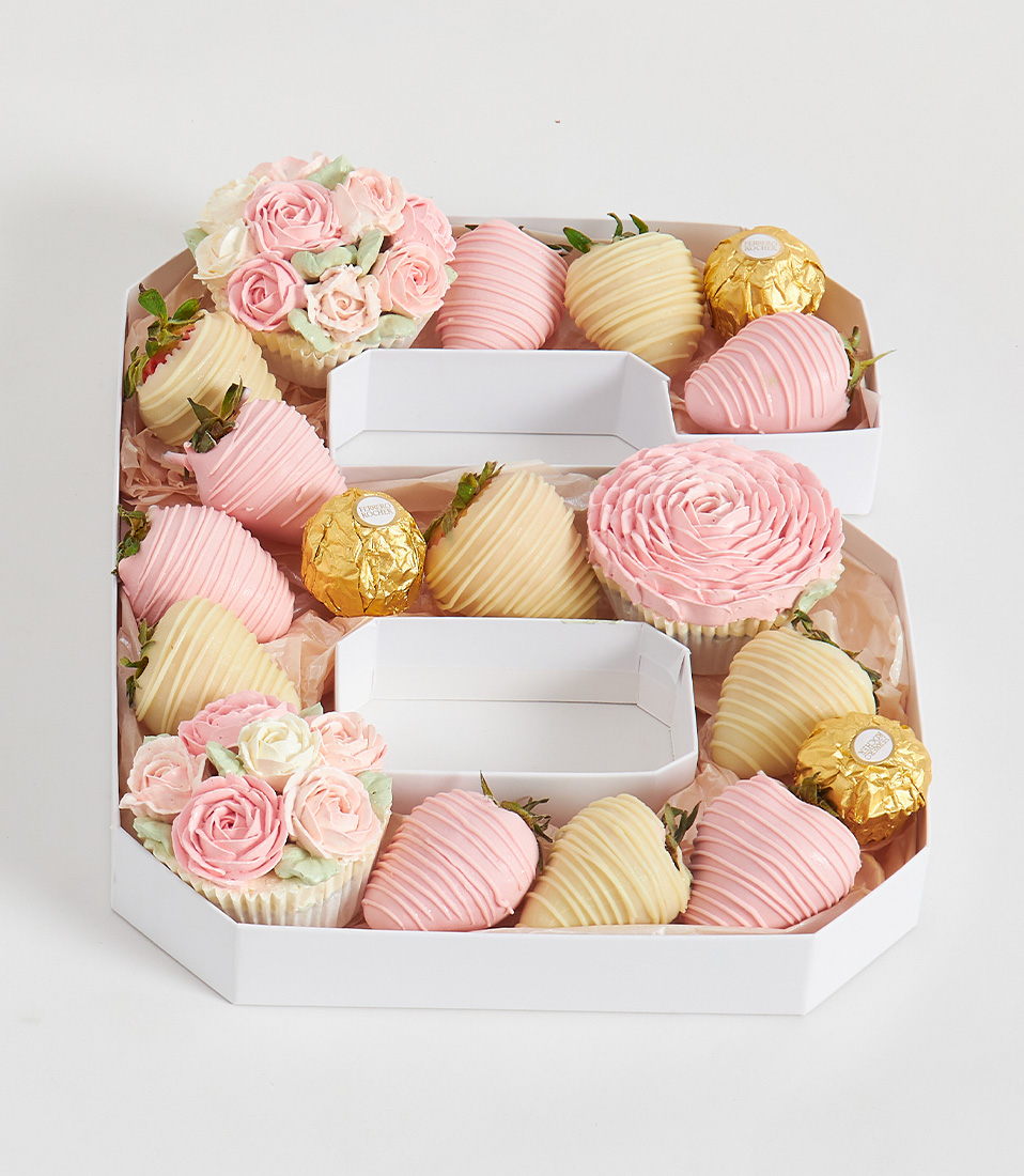 Number 6 box with pastel chocolate strawberries, pink flower cupcakes, and Ferrero Rocher in soft tones on a white background