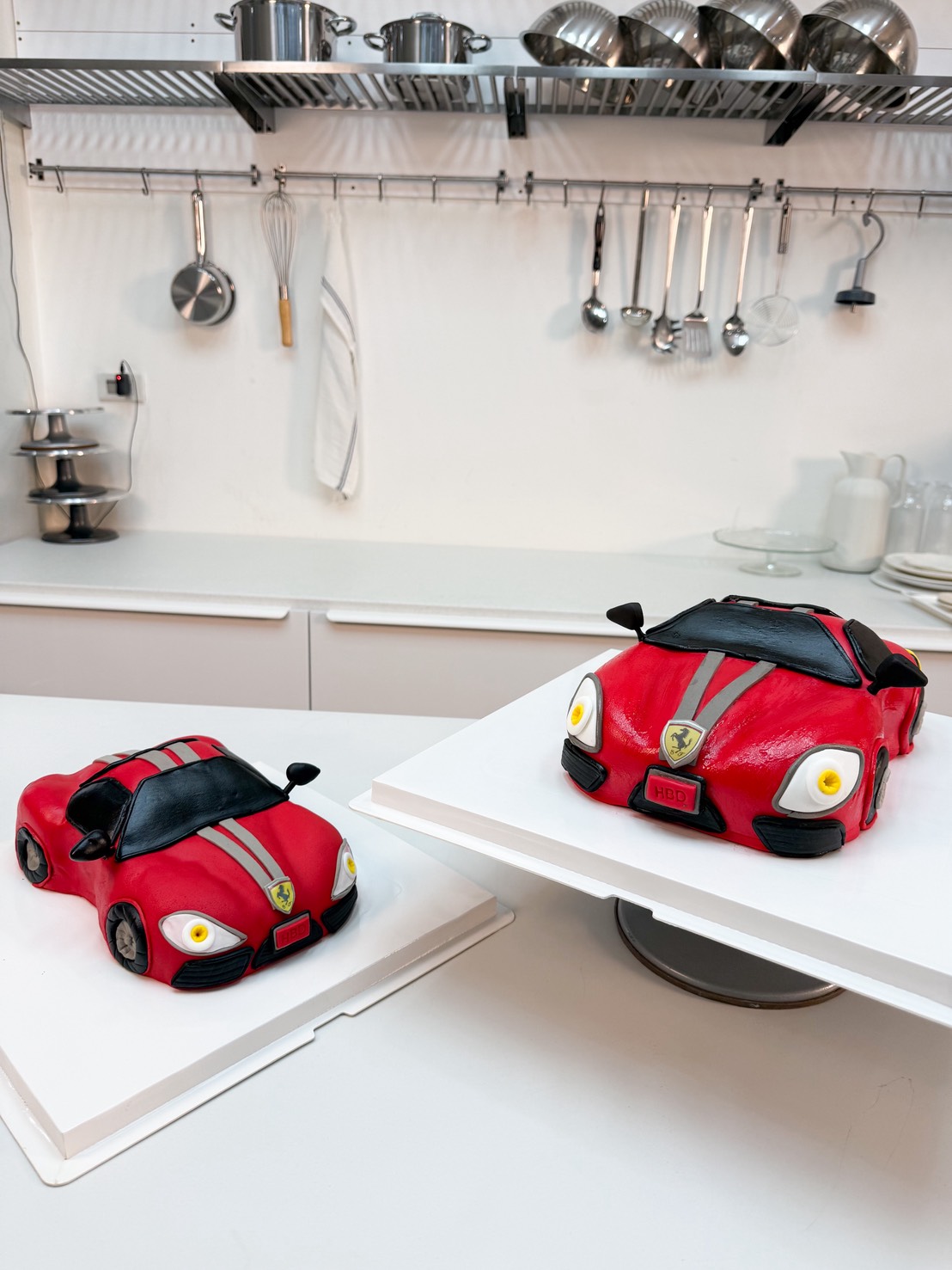 3D red sports car birthday cake with grey racing stripes, handcrafted details, on a white cake board with chocolate “Happy Birthday” message.