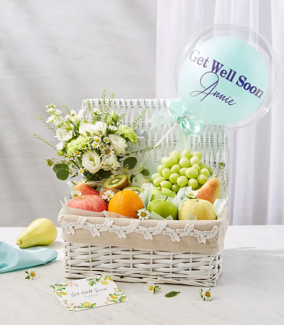 White wicker basket with fresh fruits, white-green flowers, and Get Well Soon balloon on a white background