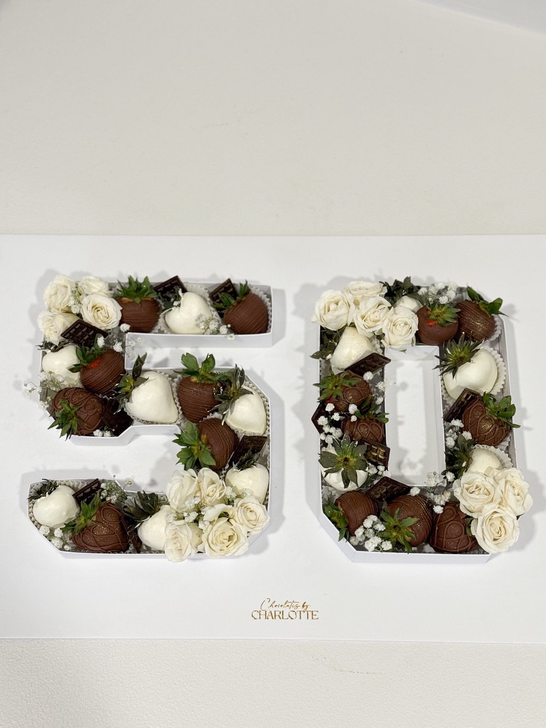 Chocolate covered strawberries arranged in number 50 box with fresh white roses for 50th birthday celebration.