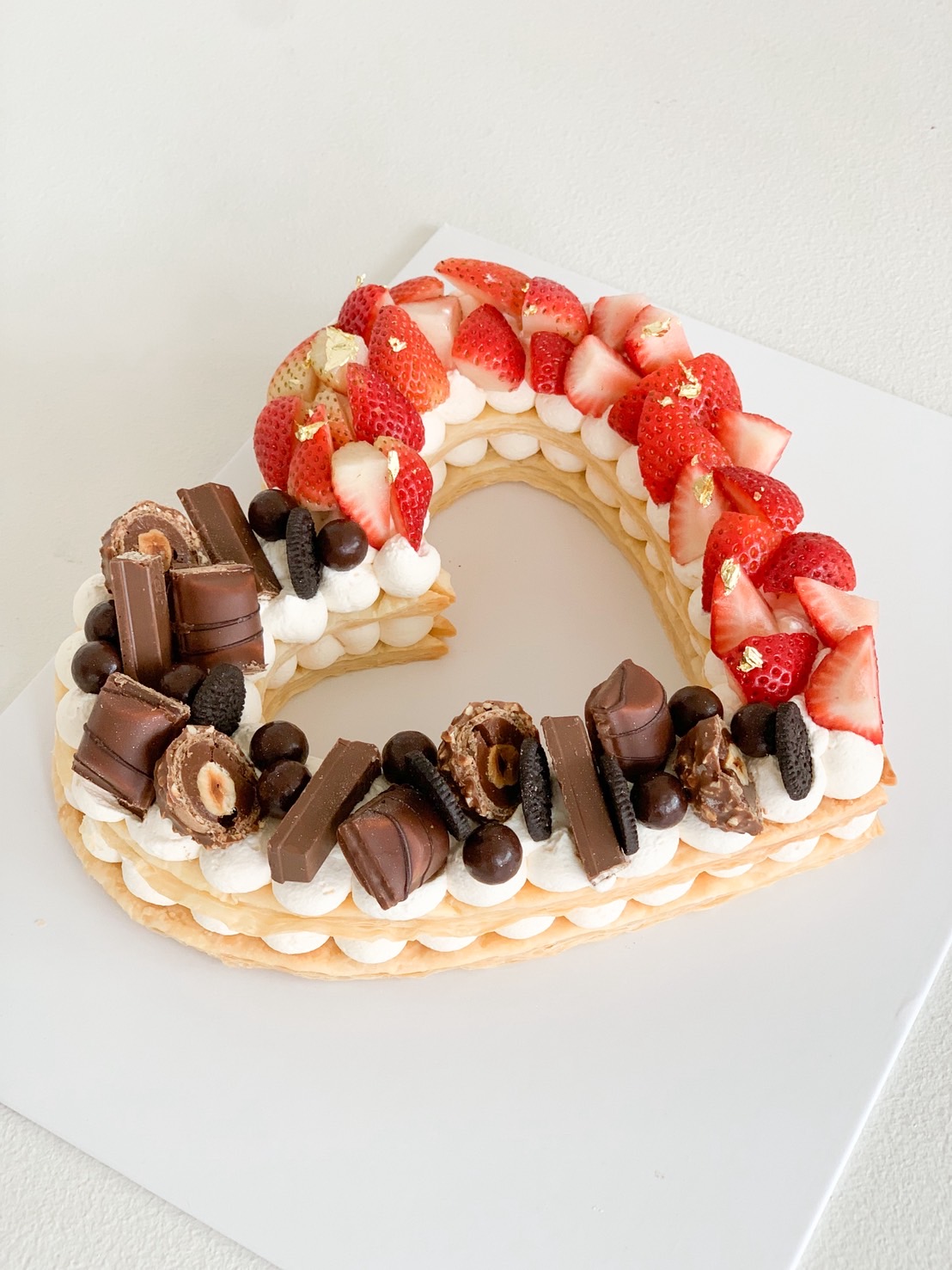 Heart-shaped cookie cake with Belgian chocolates and fresh strawberries, side angle on white board.