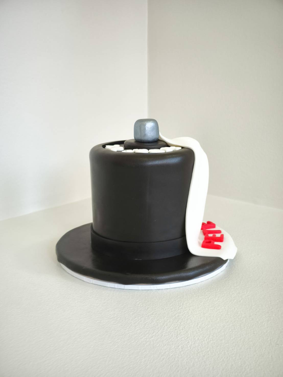 Black fondant cake shaped like a top hat with a white scarf and silver knob detail.