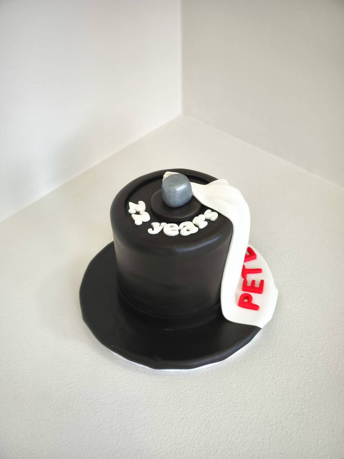 Black fondant cake shaped like a top hat with “21 years” lettering and a white scarf reading “PETV”.