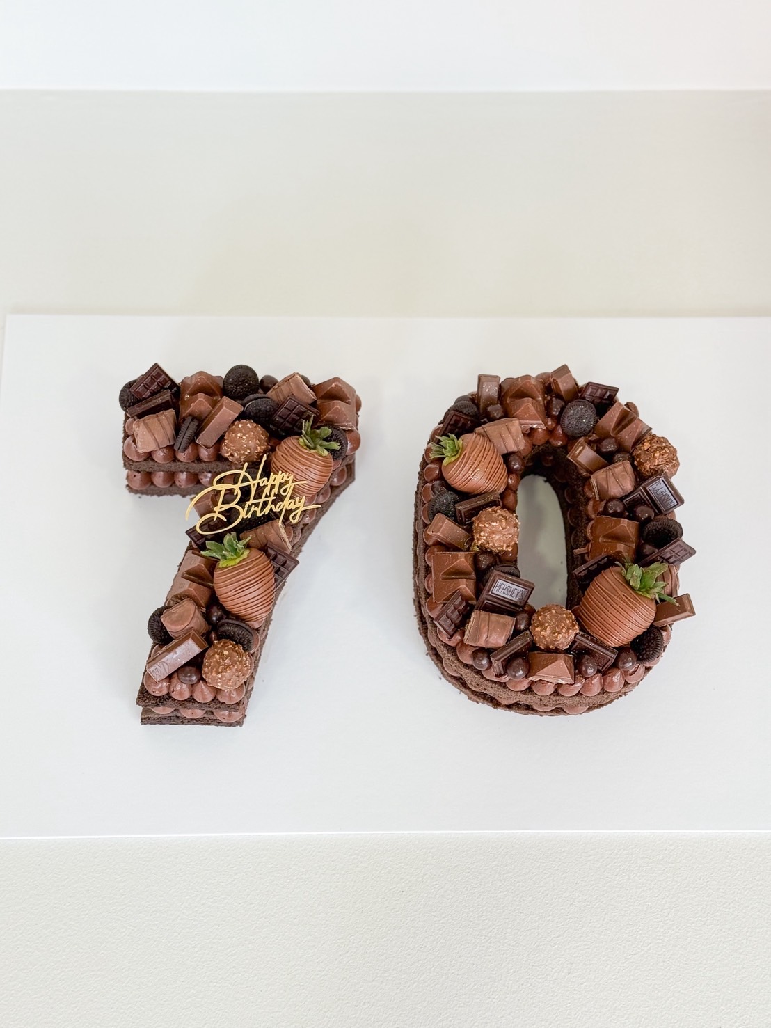 Number 70 birthday cake decorated with assorted chocolates, Ferrero Rocher, and chocolate-covered strawberries.