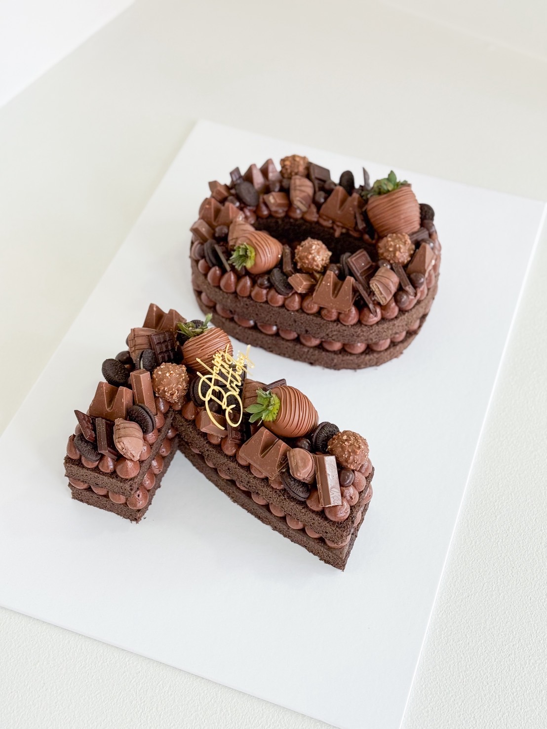 Chocolate birthday cake shaped as the number 70, topped with assorted chocolates, Ferrero Rocher, and chocolate-covered strawberries.