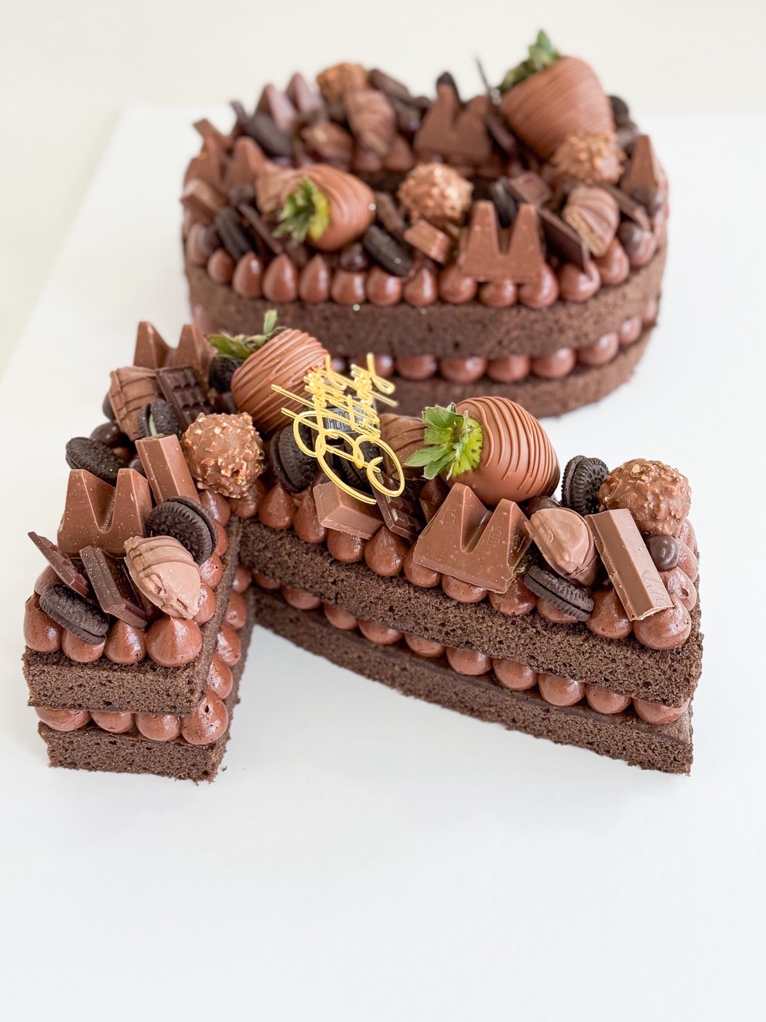 lose-up of a chocolate birthday cake topped with assorted chocolates, Ferrero Rocher, and chocolate-covered strawberries.
