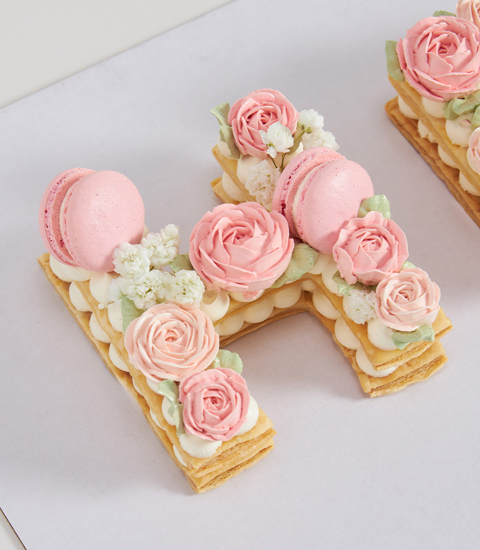Close-up of H-shaped pie cake with rose cream and macarons