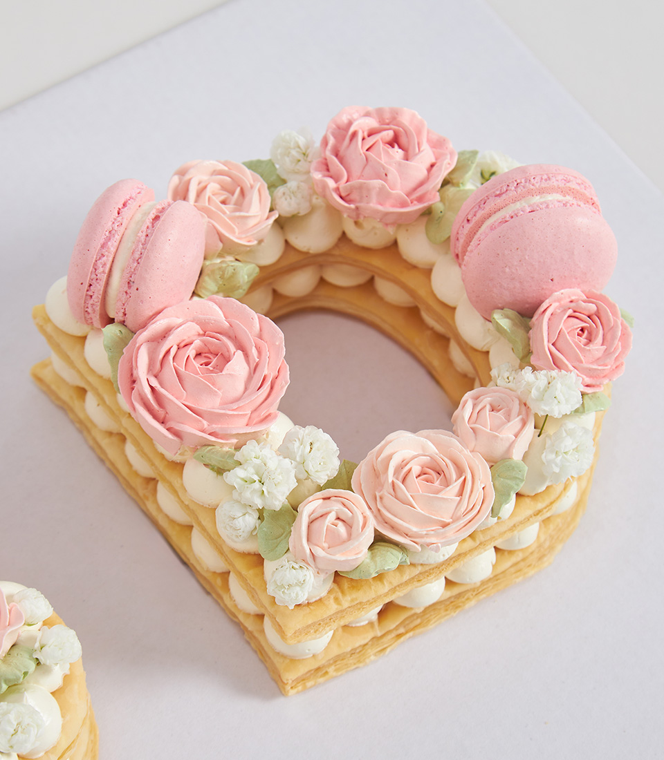 D-shaped pie cake topped with pink rose buttercream and pastel macarons