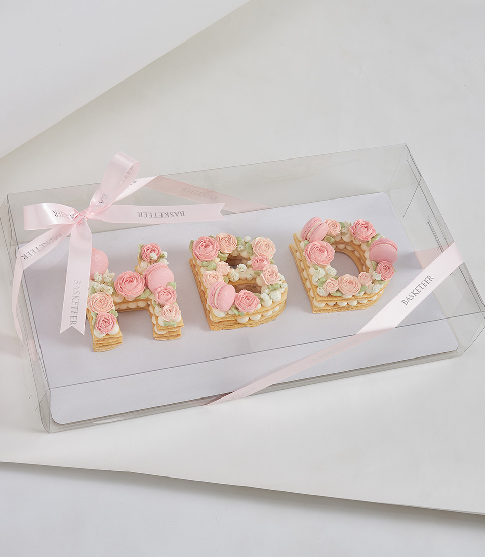 Letter-shaped puff pie cake decorated with pink buttercream flowers and macarons