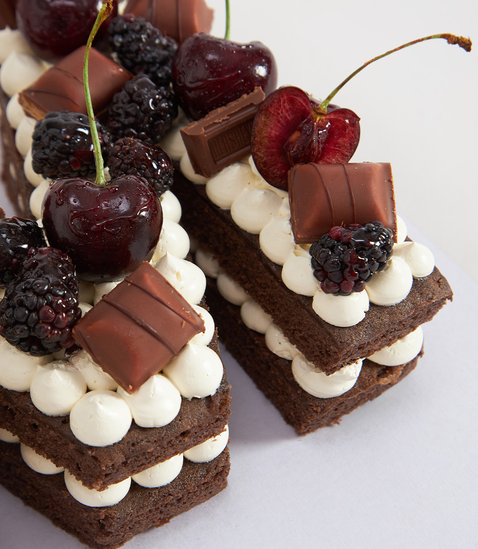 Close-up of a Letter-shaped chocolate sponge cake topped with cherries, blackberries, and premium chocolates