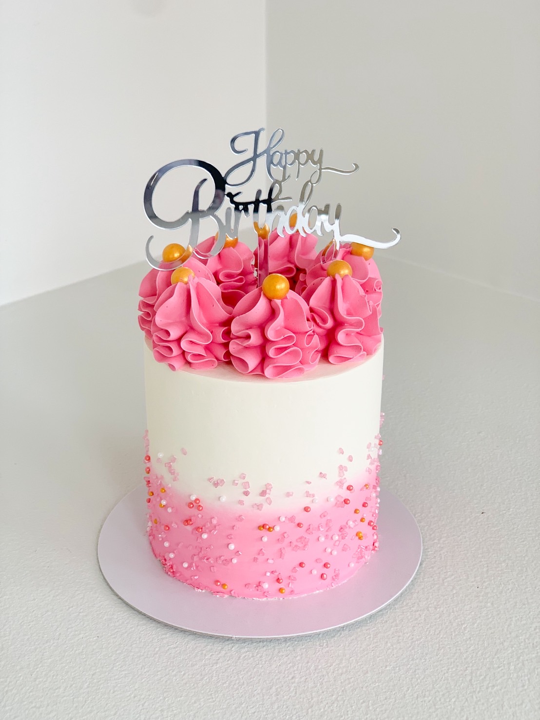 Pink ombre birthday cake with silver Happy Birthday topper and gold pearls.