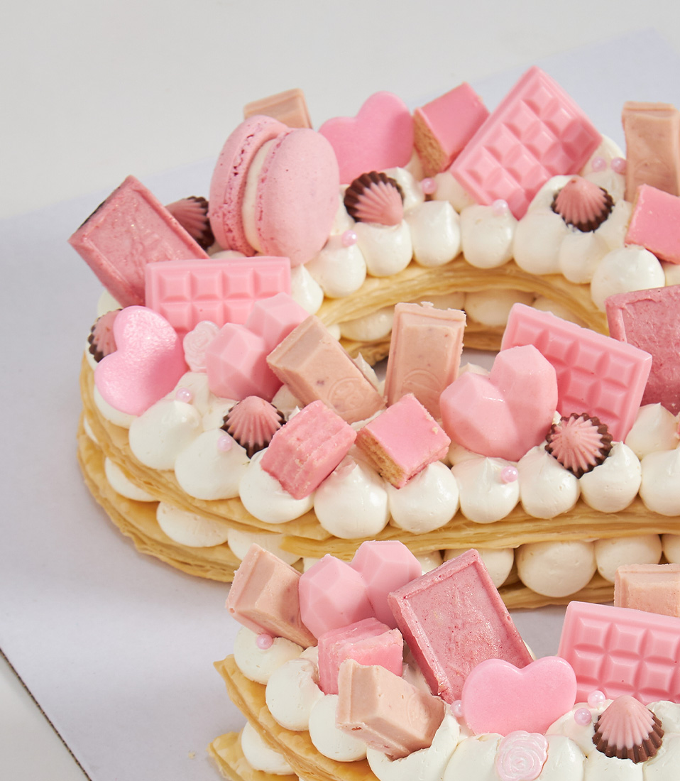 Close-up of a Pink puff letter cake decorated with assorted pink chocolates, mini macarons, and heart-shaped confections