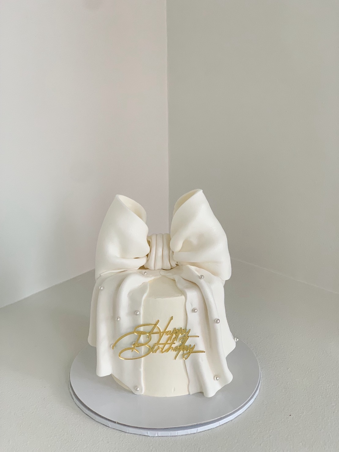 Elegant white birthday cake with large fondant bow and pearl decorations.