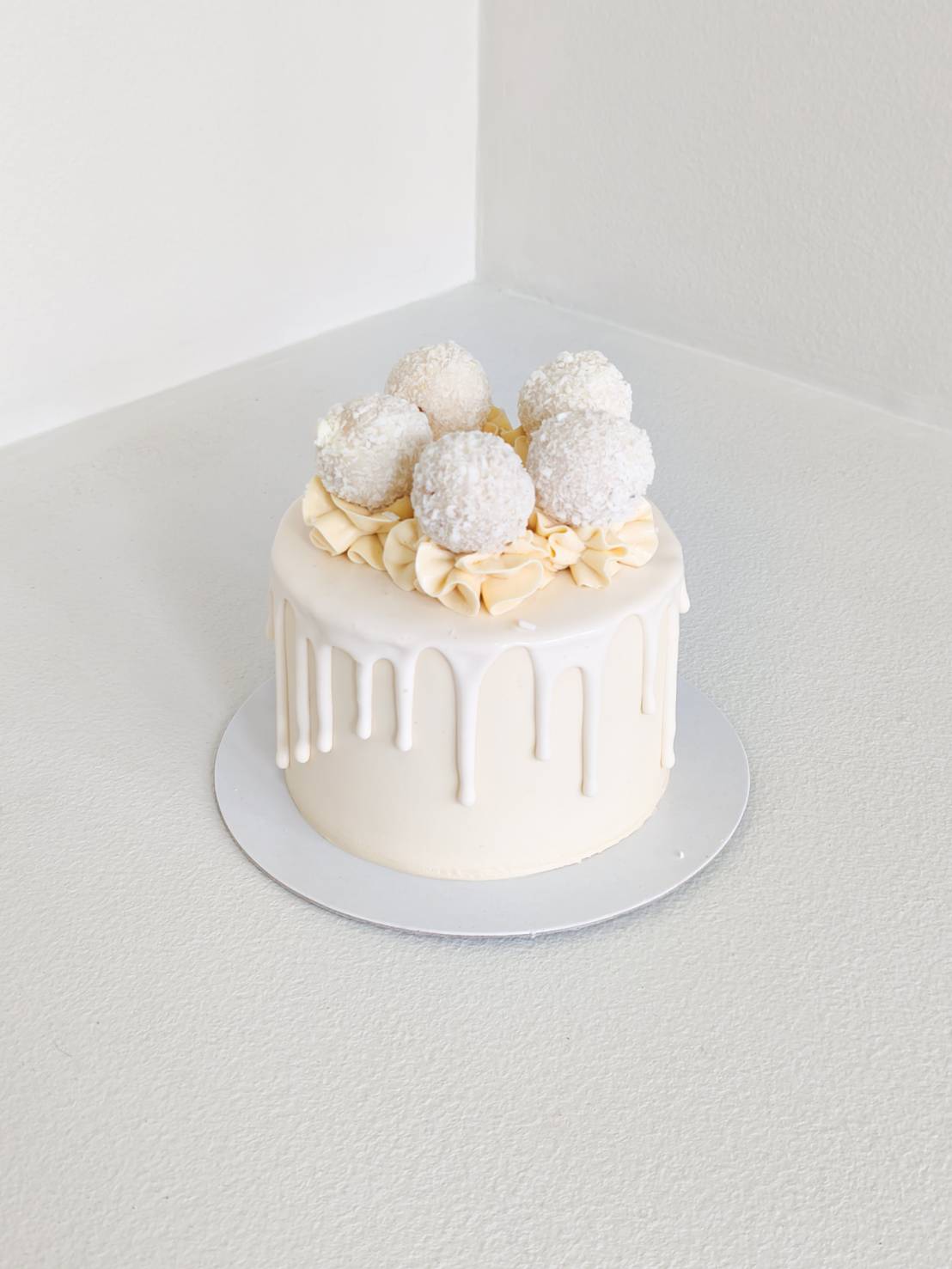 Minimalist white drip cake topped with coconut truffles and cream swirls, luxury birthday cake design.