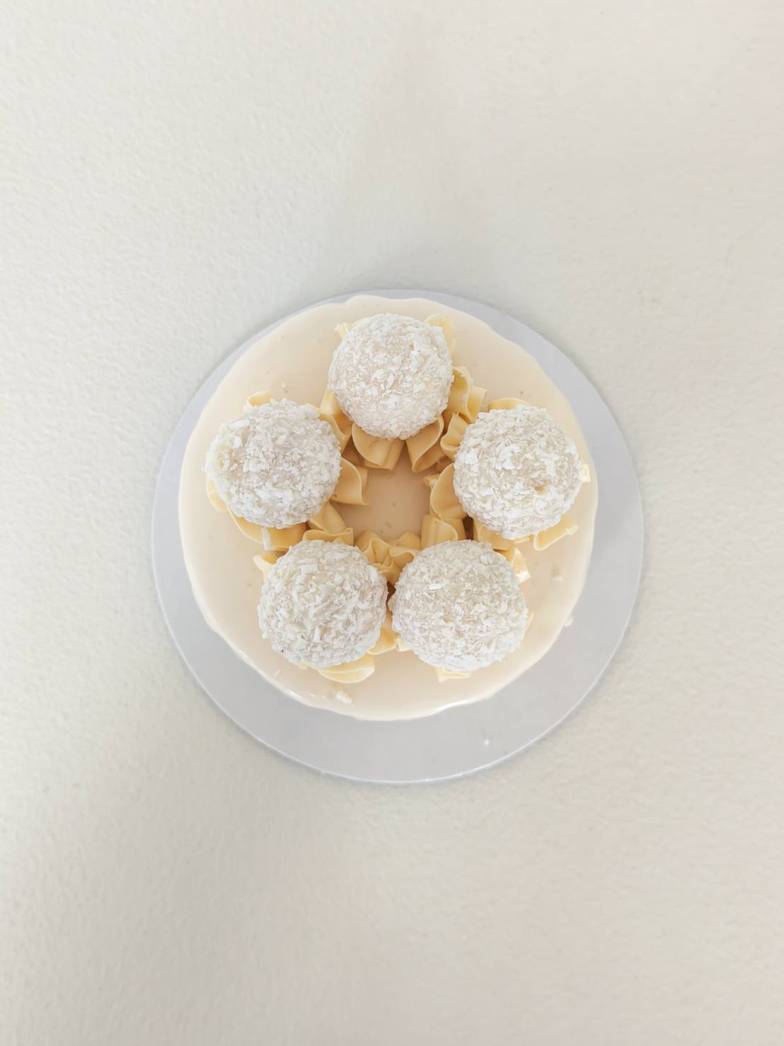 Top view of minimalist white drip cake decorated with coconut truffles and cream swirls.