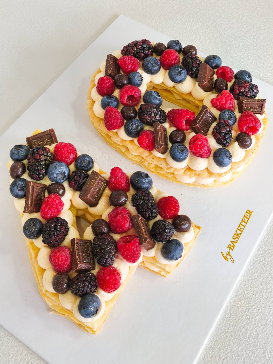 Custom letter cake decorated with fresh blueberries, raspberries, blackberries, and premium chocolate pieces.