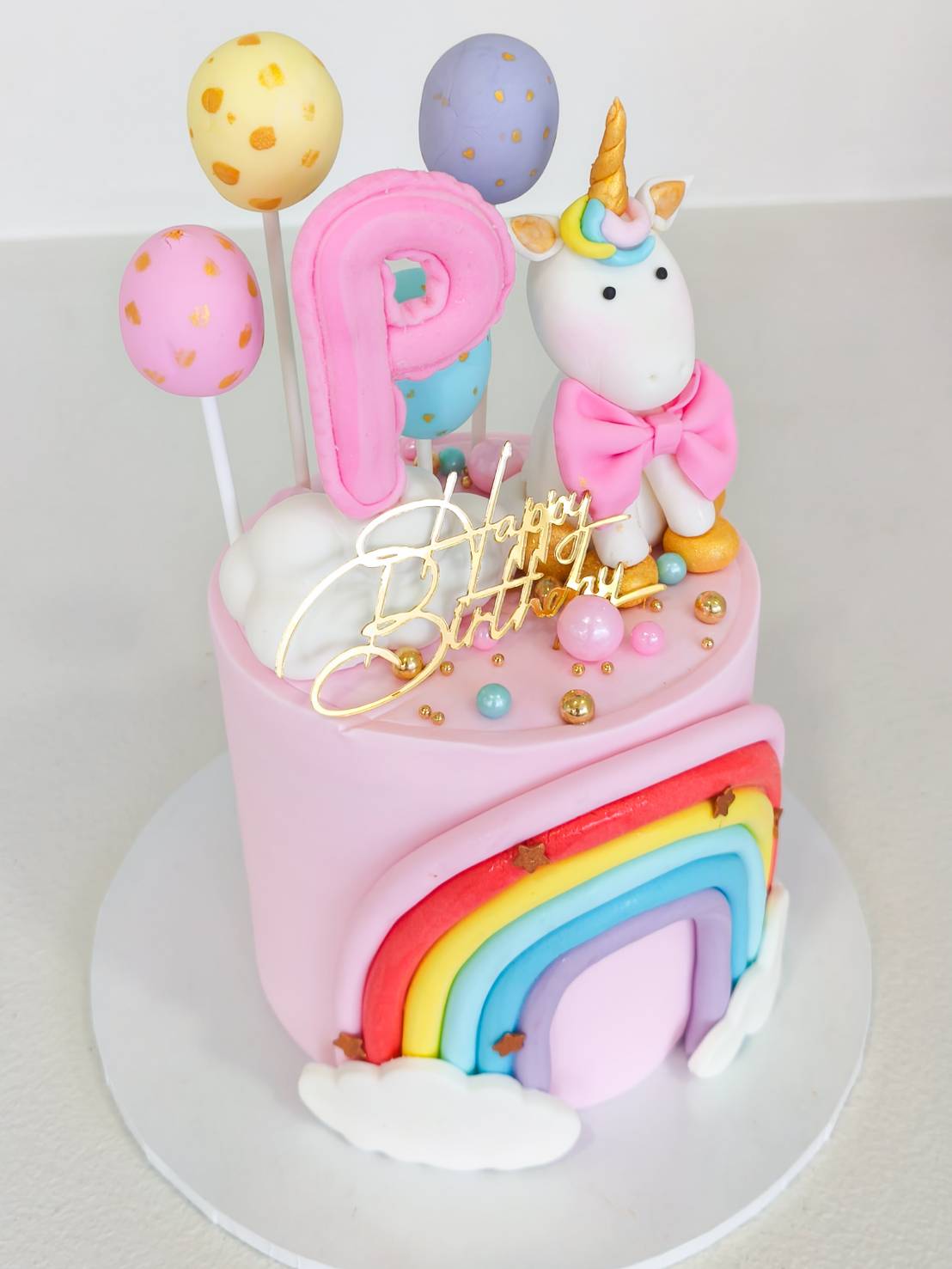 Pink unicorn birthday cake decorated with rainbow, balloons, and fondant unicorn topper, perfect for kids’ celebrations.