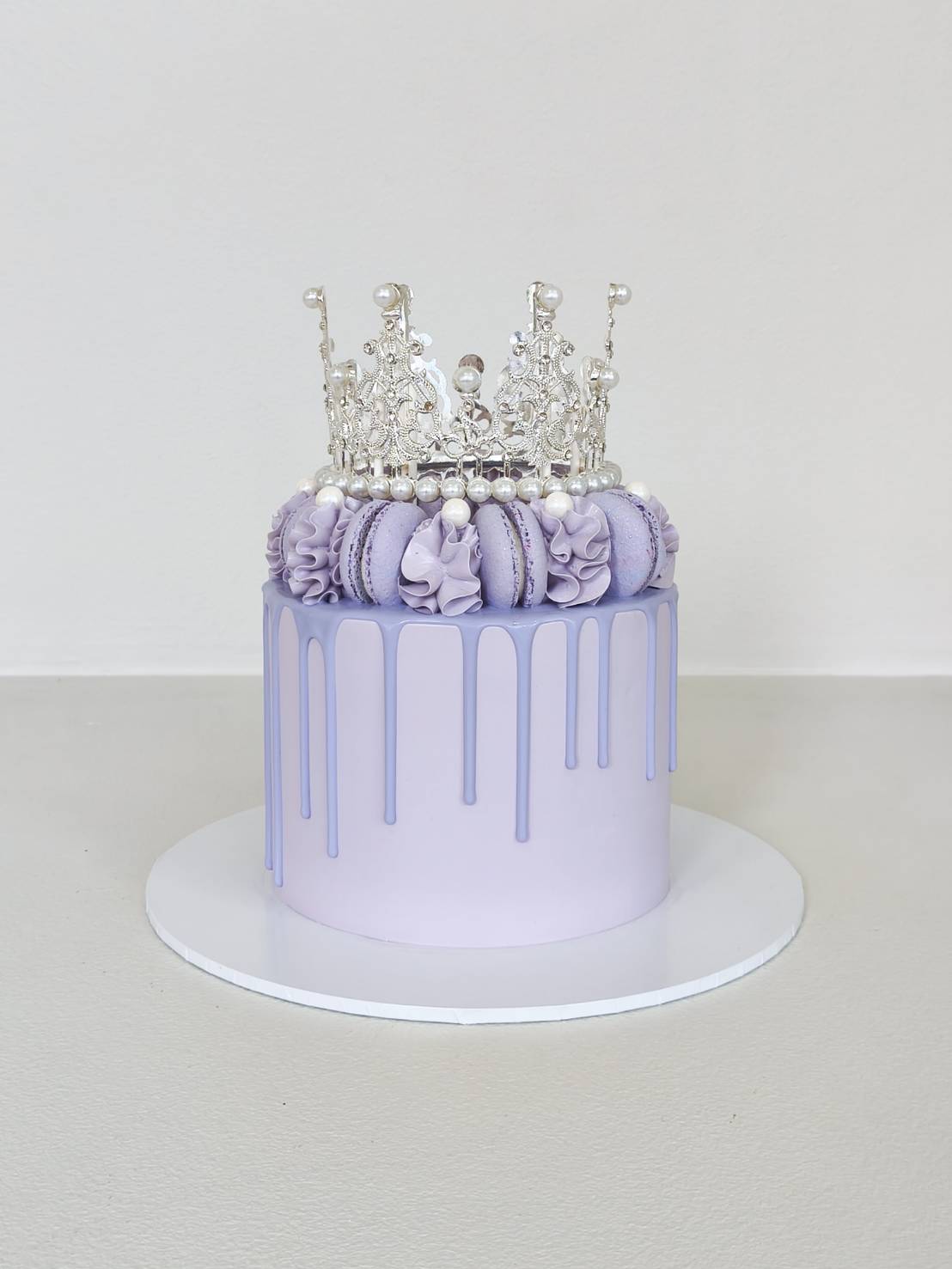 Elegant lavender cake with silver crown topper, decorated with macarons, pearls, and ruffle cream details.