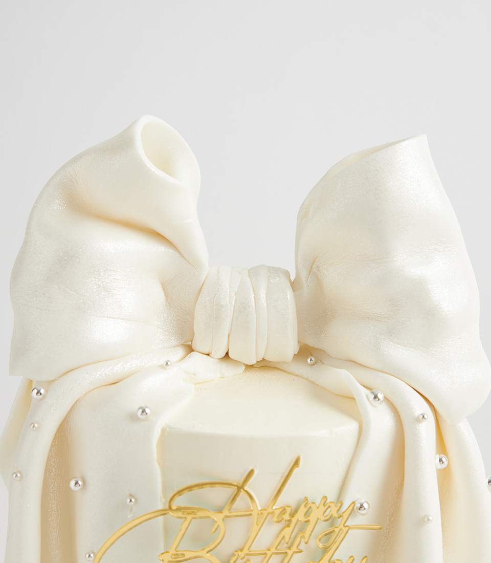 Close-up of shimmering white fondant bow with pearl accents on luxury cake