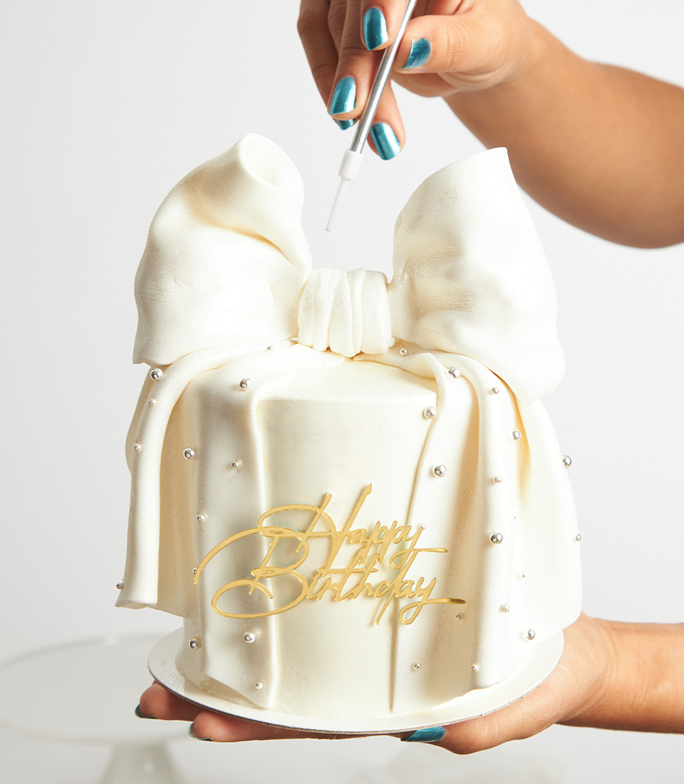 Close-up of luxury white bow cake with edible pearls being hand-decorated