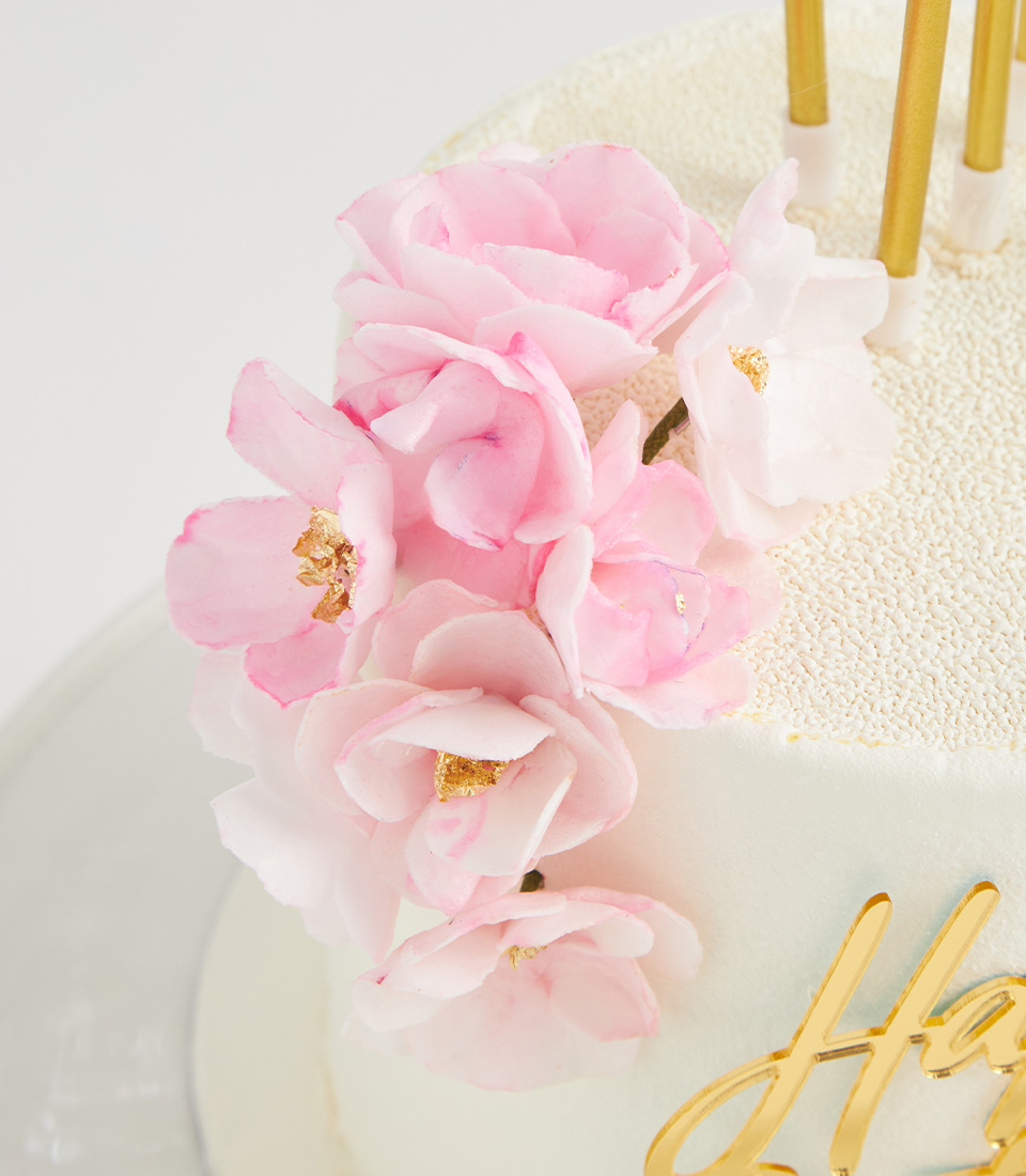 Close-up of pink and white edible flowers with gold accents on a white birthday cake