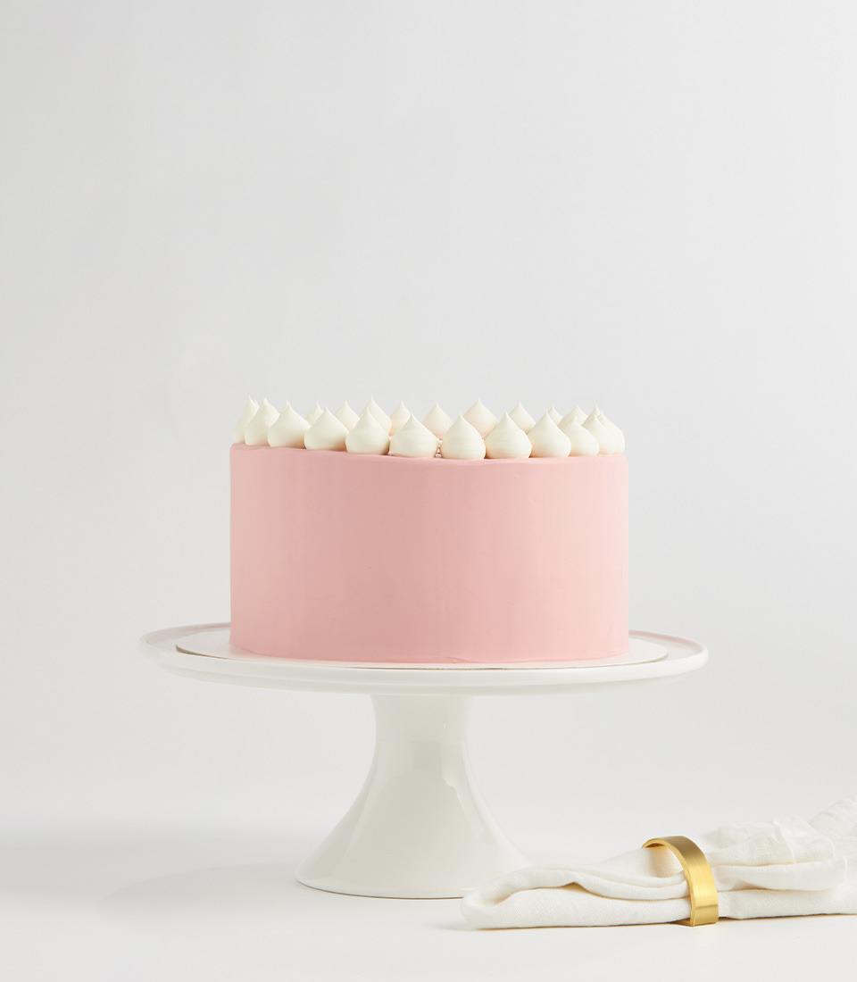 Pink frosted vanilla cake topped with white buttercream puffs