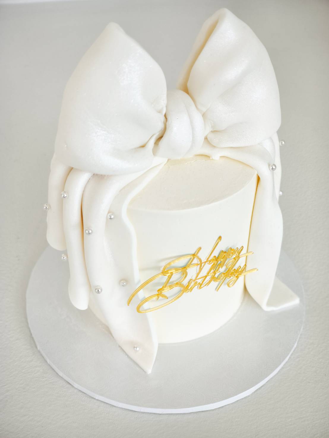 Minimalist white birthday cake decorated with a large fondant bow and pearls
