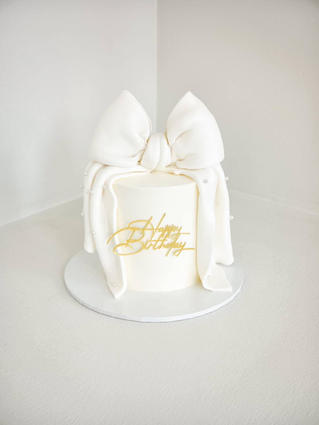 Elegant white birthday cake with a large fondant bow and pearl decorations