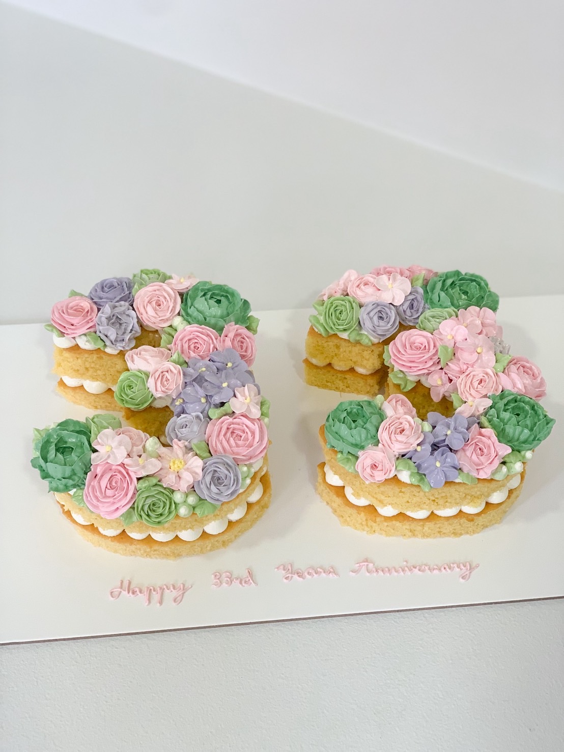 Buttercream flower number cake in the shape of 33, decorated with pastel floral icing and piped cream layers.