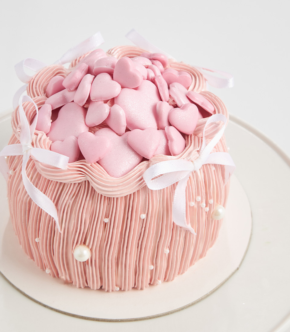 Pink dome cake topped with fondant hearts, bows, and edible pearls