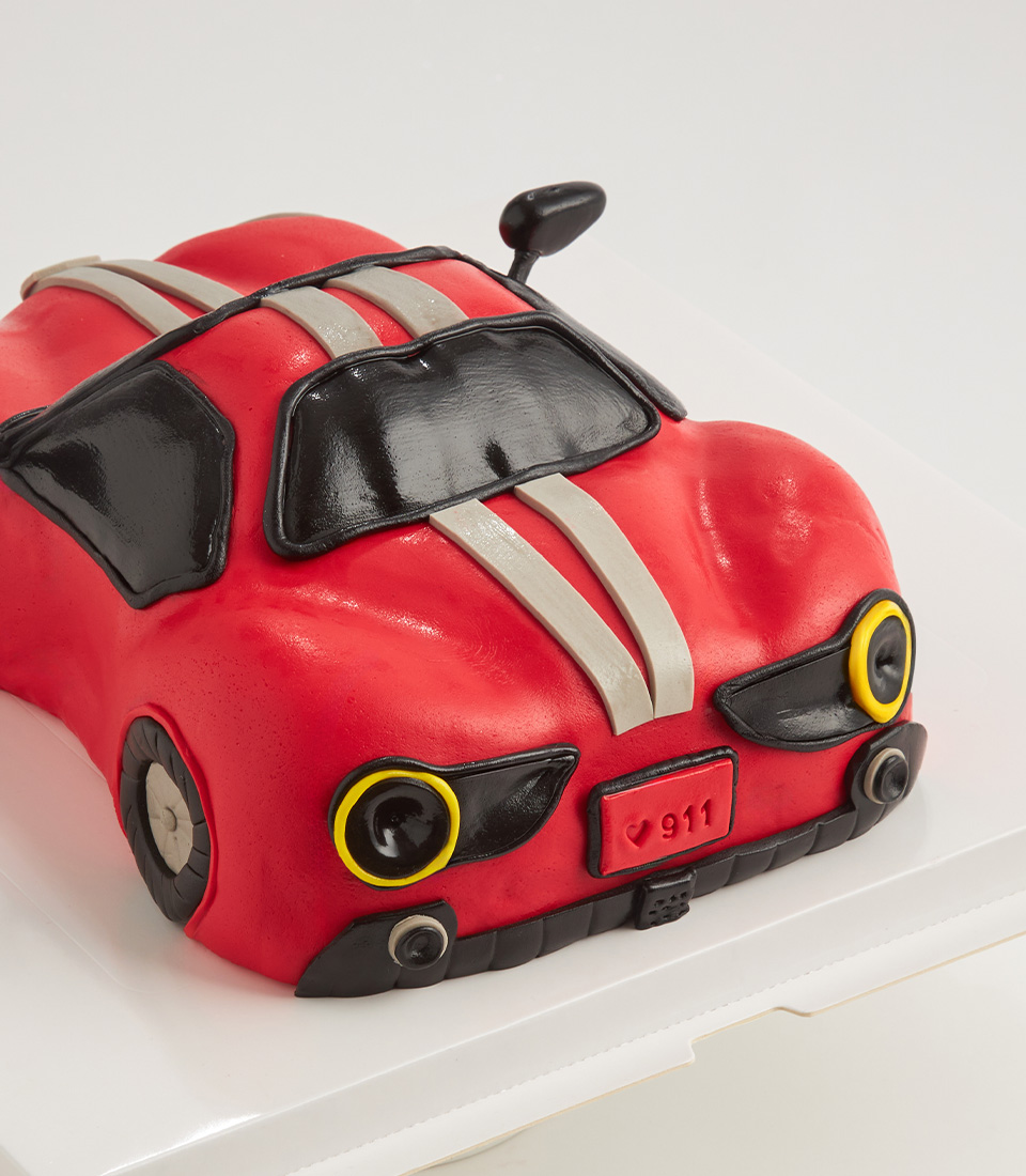 Red sports car-shaped cake decorated with fondant details, headlights, windows, and racing stripes.