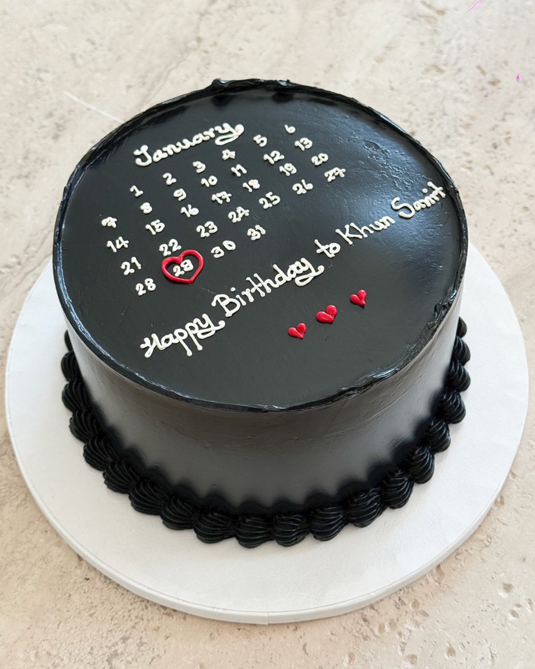 A round black frosted Anniversary Calendar Cake displays a January calendar with the 22nd circled in red. The cake reads 