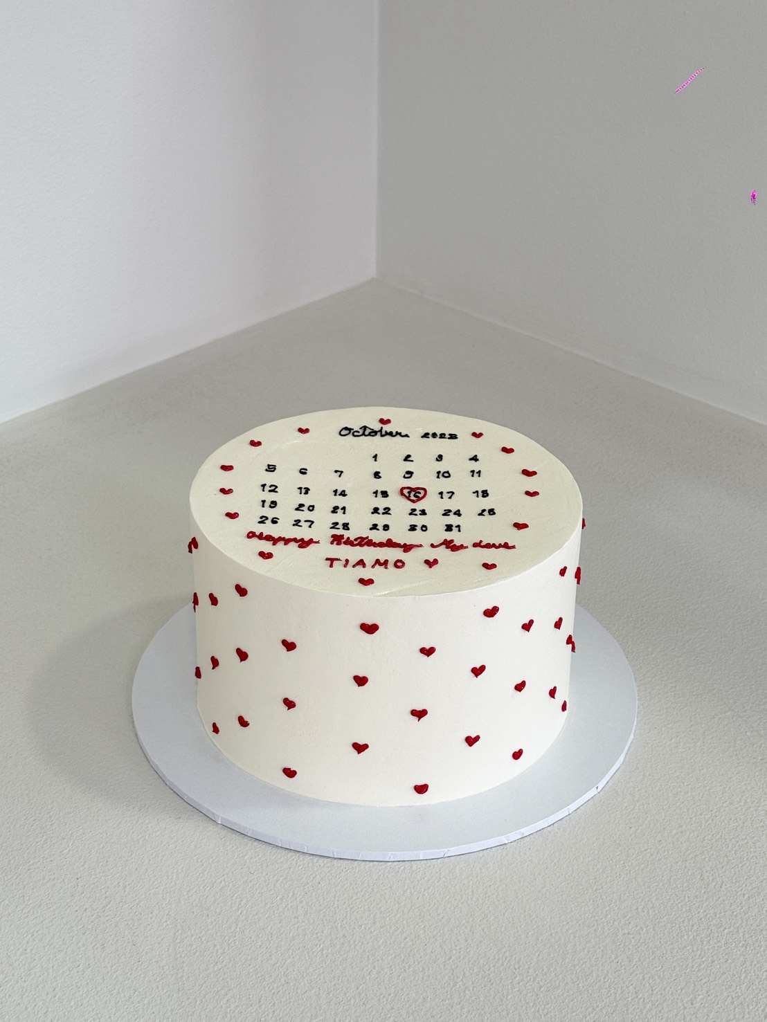 A Sweet Calendar Cake: a round white cake adorned with red hearts and an October 2023 calendar on top. A heart marks the 14th, with 