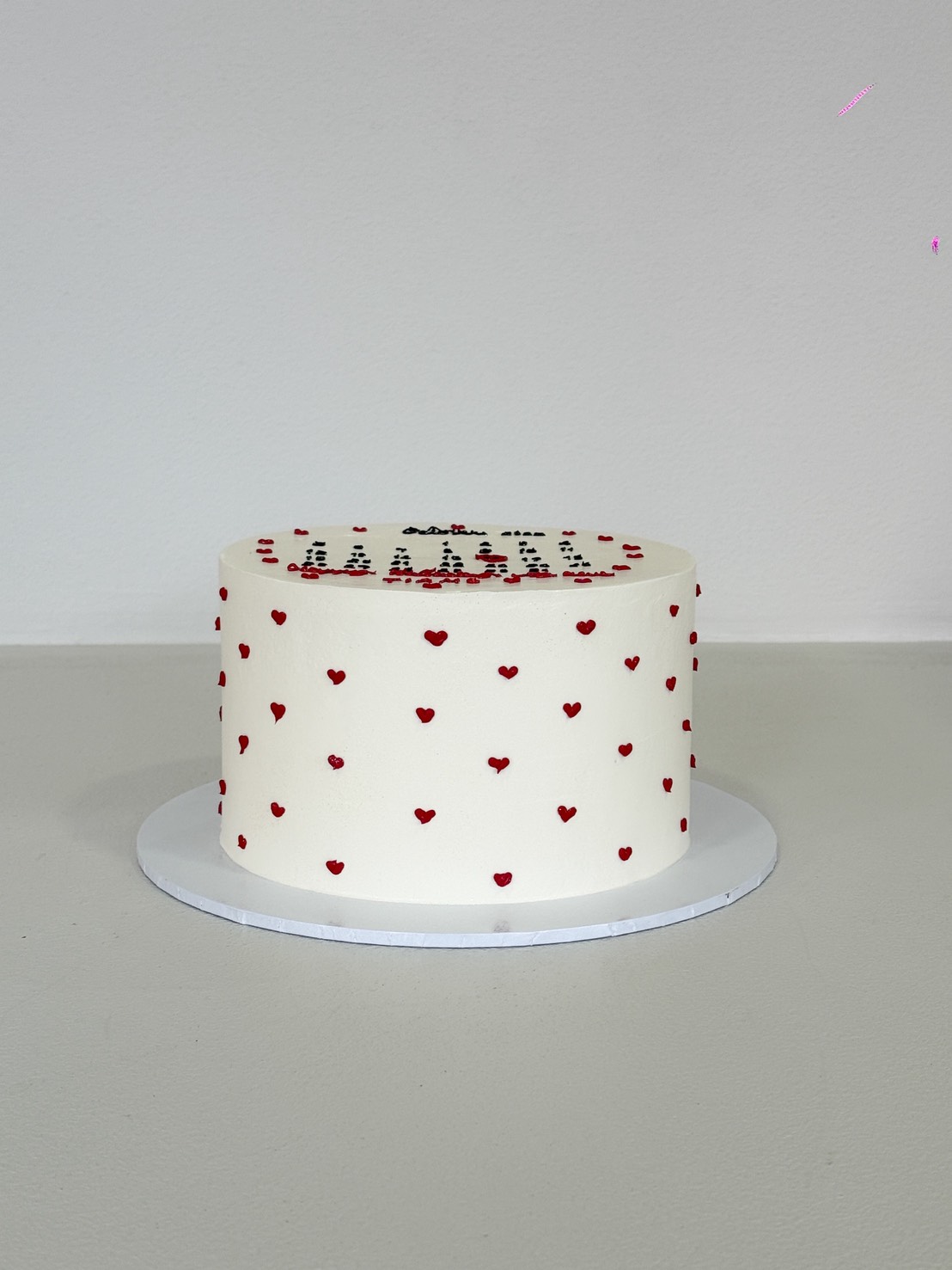 A round white Sweet Calendar Cake decorated with small red heart shapes, sitting on a white cake board against a plain light background.