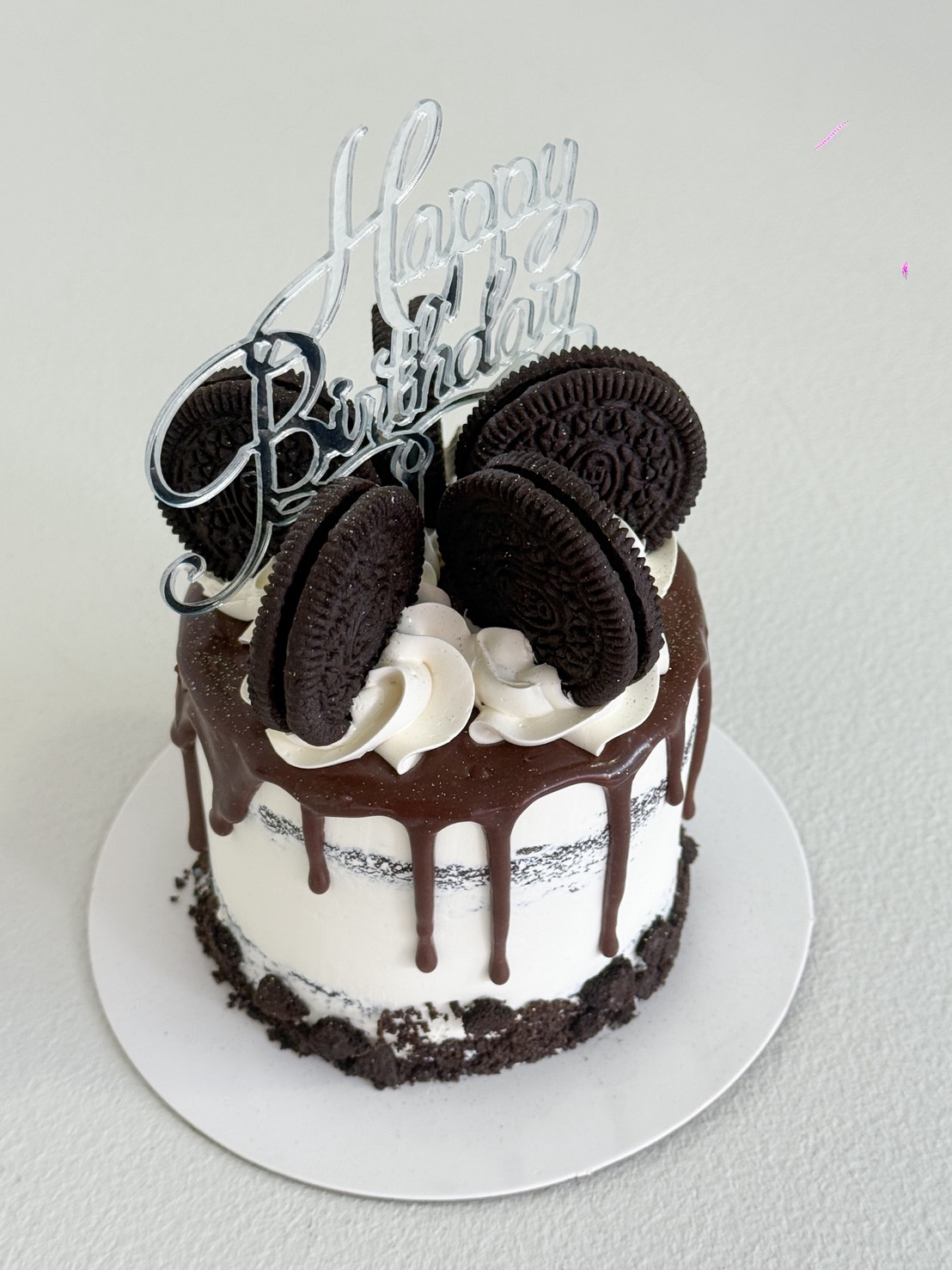 A small, round Rich Oreo Cream Cake with chocolate drip icing, white icing, Oreo biscuits on top, and a silver 