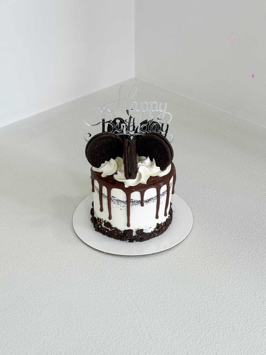 A Rich Oreo Cream Cake featuring chocolate drip, white icing, Oreo biscuits, and a silver 