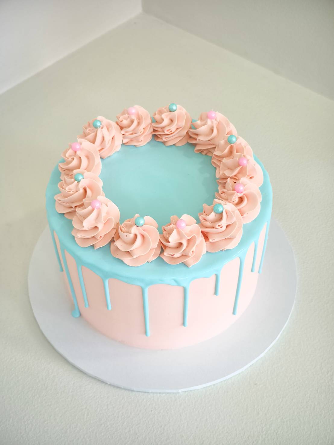 Pastel pink cake with blue drip design, topped with pink swirls and pastel pearls.