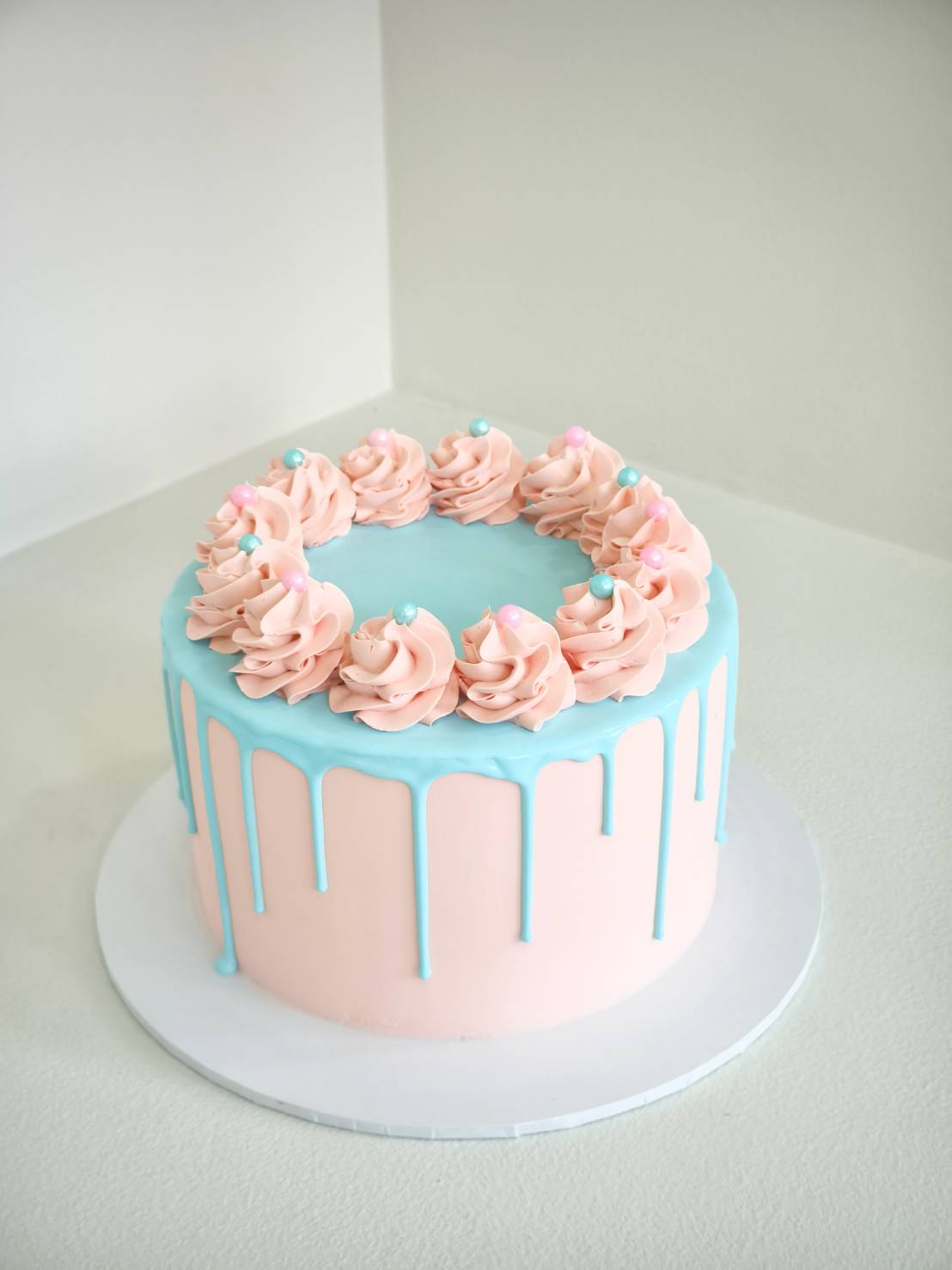 Pastel pink cake with blue drip, decorated with pink swirls and pastel sugar pearls.