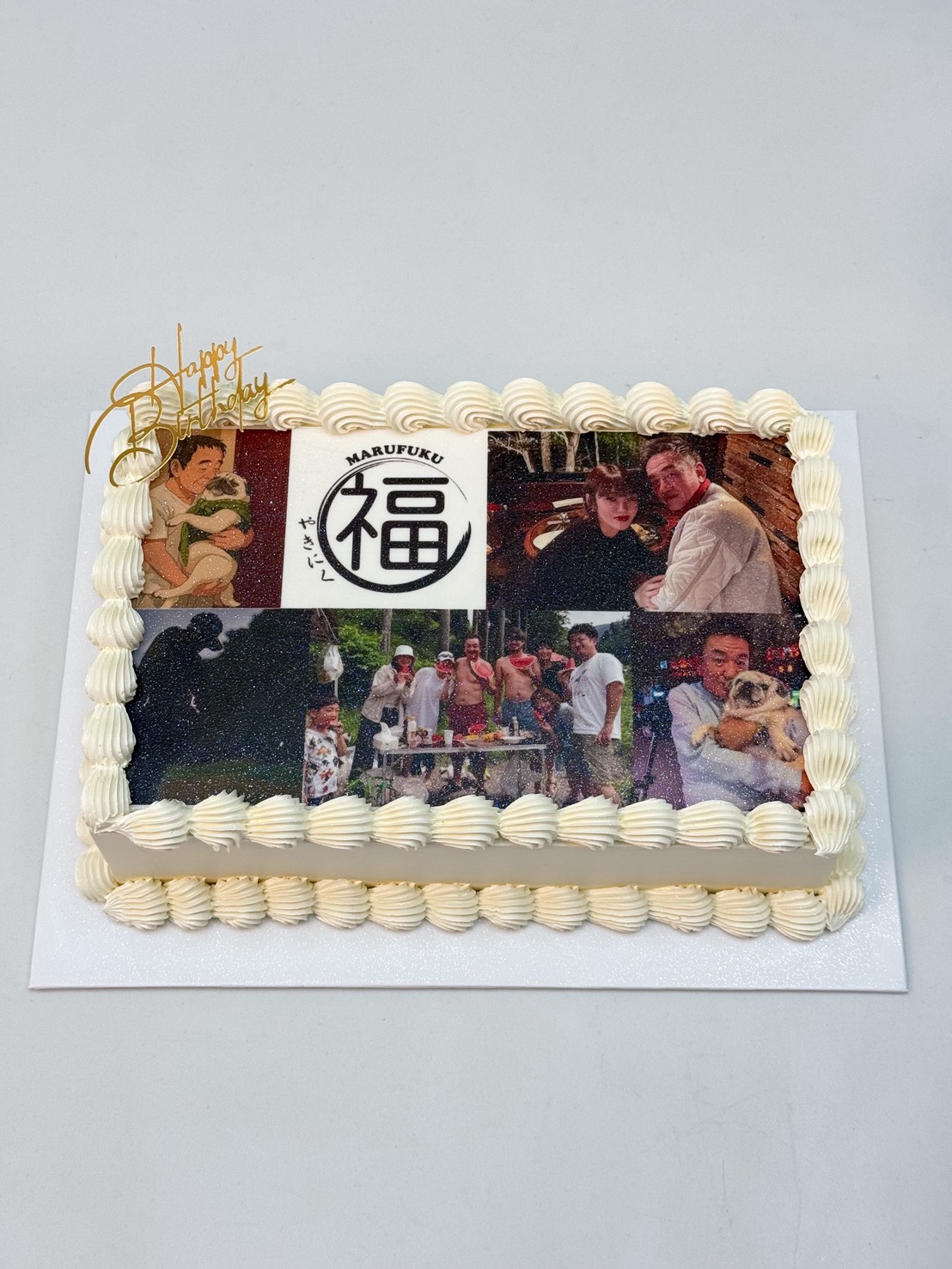 A rectangular personalised vanilla edible photo cake with white icing features edible images of people, a child and a dog, a circular symbol with Japanese characters, and a gold 