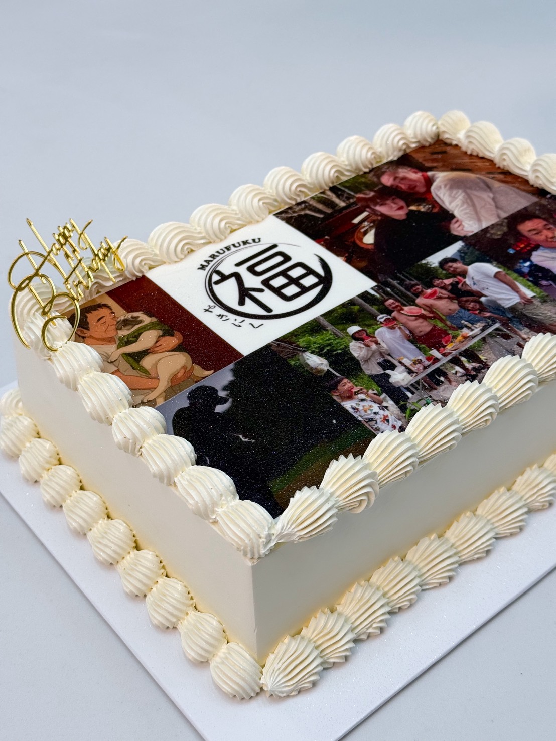 Rectangular white iced Personalised Vanilla Edible Photo Cake with piped borders, decorated with printed edible photos of people and a central circular symbol. A gold “Happy Birthday” topper is placed at the corner.