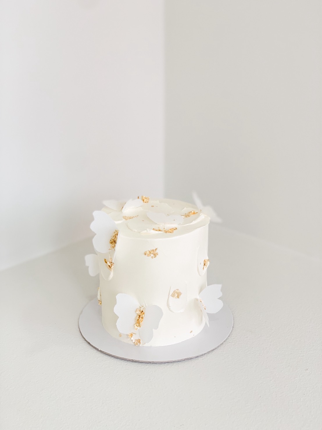 Elegant minimalist white cake with delicate white butterfly toppers and gold leaf accents.