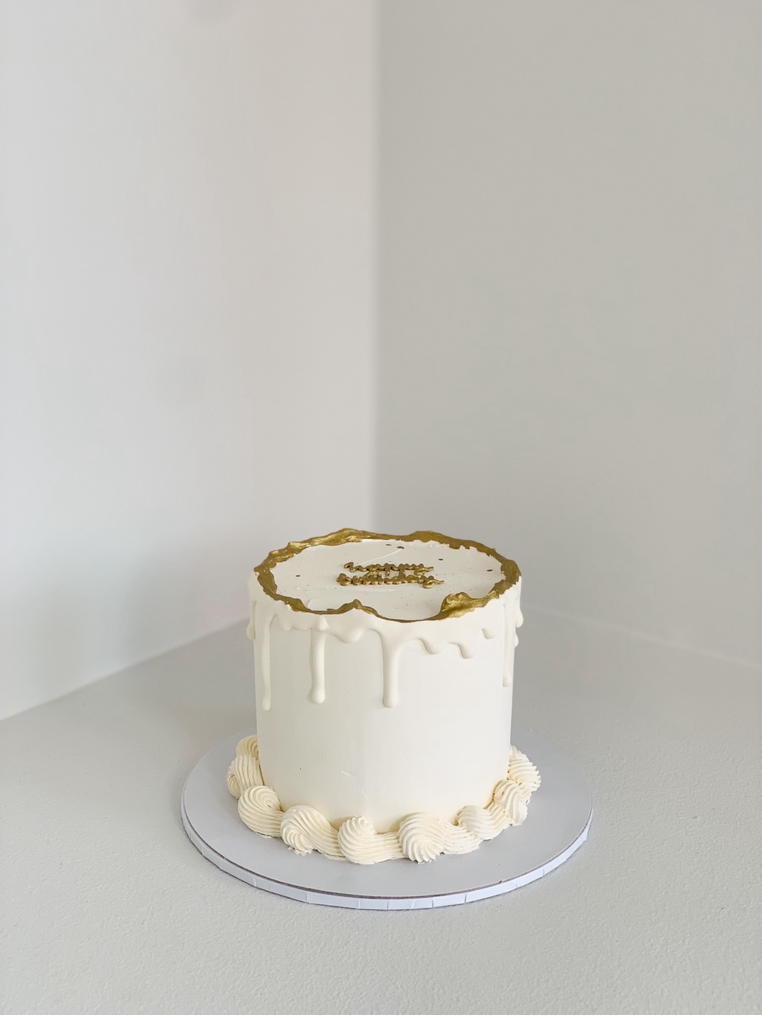 Minimal white birthday cake with gold accents and buttercream drip design, elegant tall style.