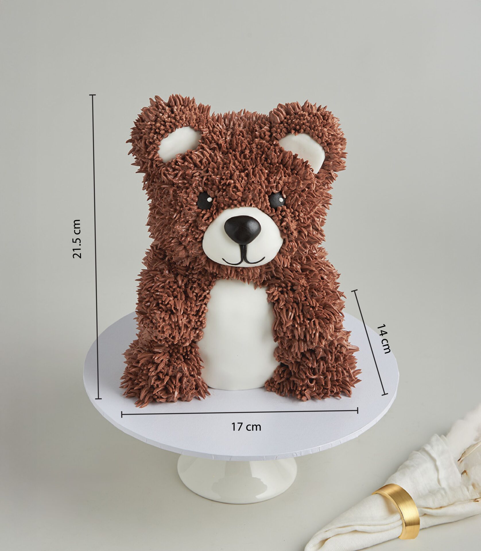 Front-facing 3D teddy bear cake with chocolate buttercream fur and fondant detailing, measuring 21.5 cm tall, 17 cm wide, and 14 cm deep.