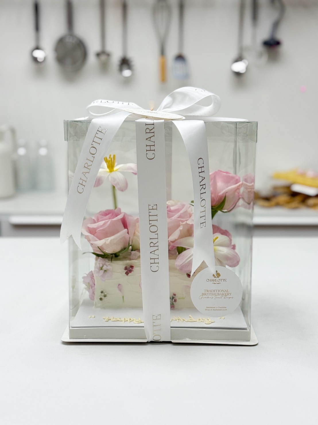 A clear gift box with white ribbon reading 