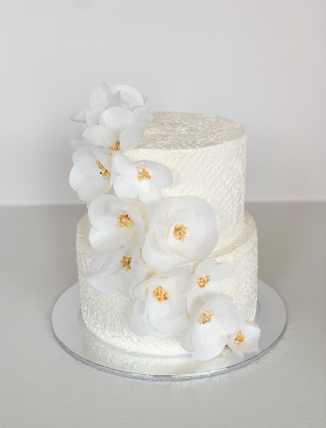 Elegant two-tier white cake decorated with white sugar orchids and gold centres
