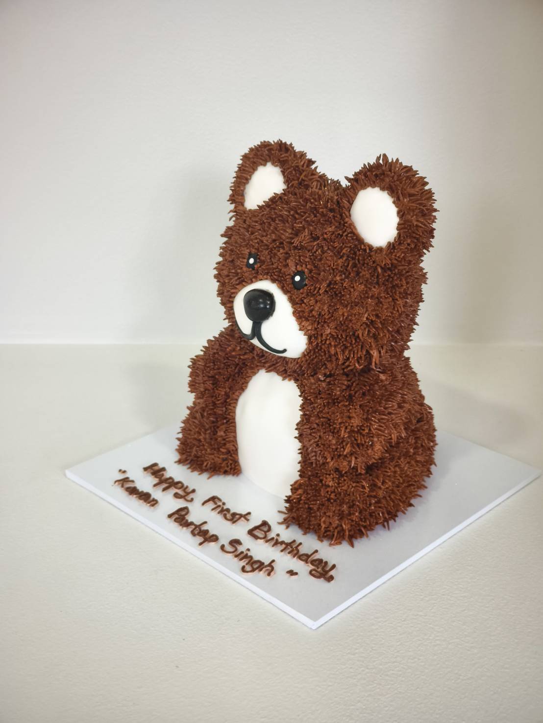 Side view of a 3D teddy bear birthday cake with chocolate buttercream piping and fondant face, designed for children